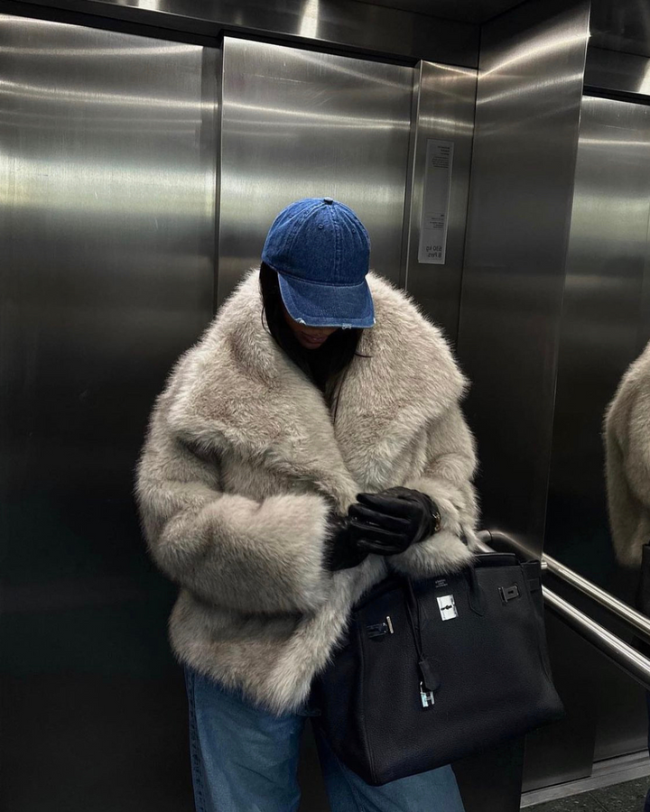 Person wearing a fur coat and blue cap inside an elevator.