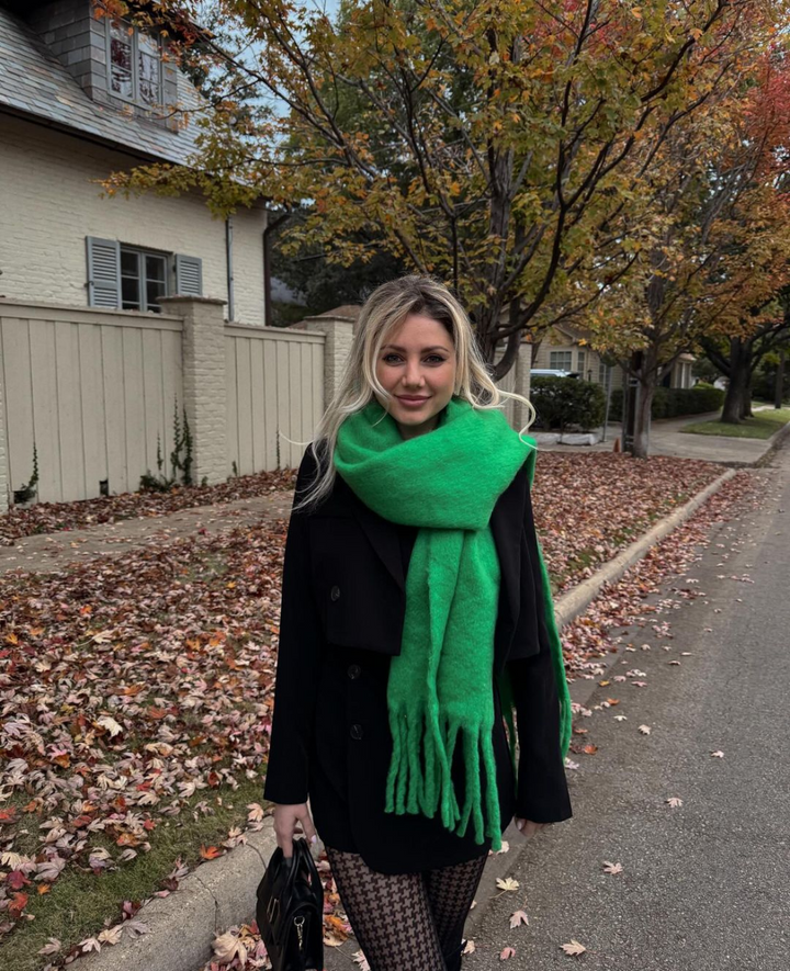 Woman wearing a green scarf in an autumn setting with fallen leaves on the ground.
