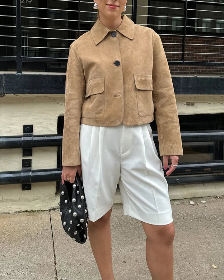 Person wearing a beige jacket and white shorts holding a polka dot bag.
