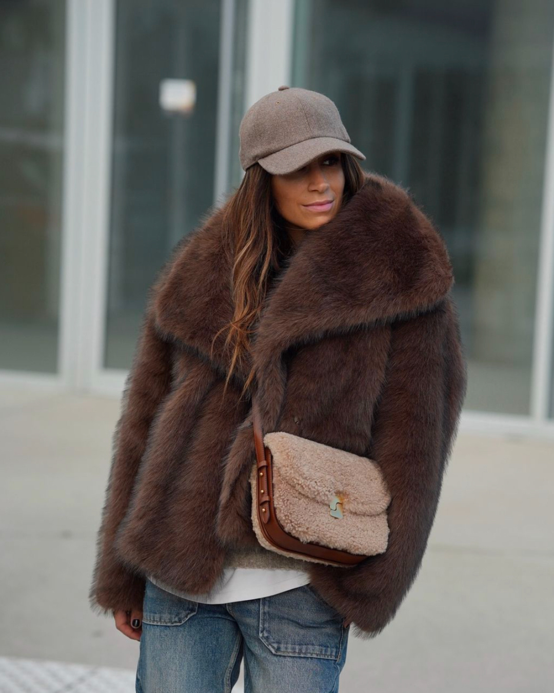 Person wearing a brown fur coat and matching hat with a matching bag, standing outdoors.