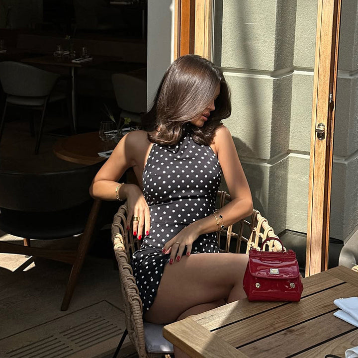 Woman in a polka dot dress sitting at an outdoor cafe table with a red handbag.