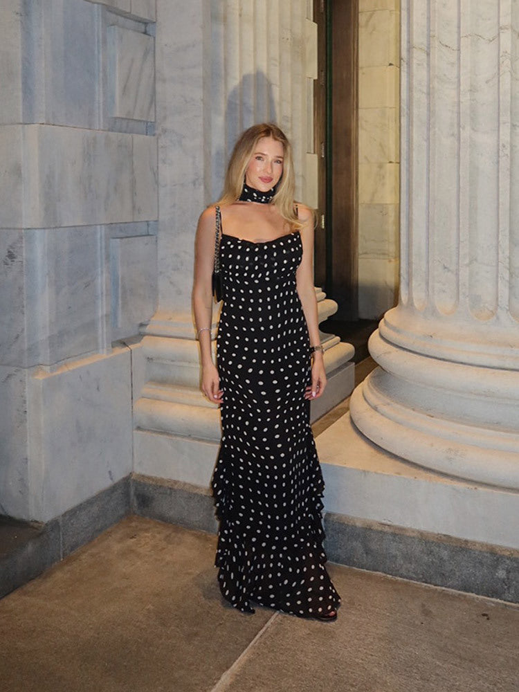 Woman in a black and white polka dot dress standing in an elegant interior setting.
