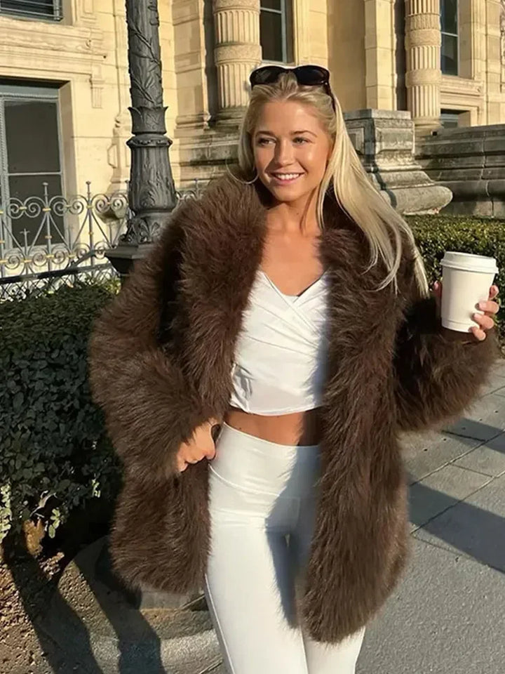 Woman in a brown fur coat and white outfit holding a coffee cup outdoors.