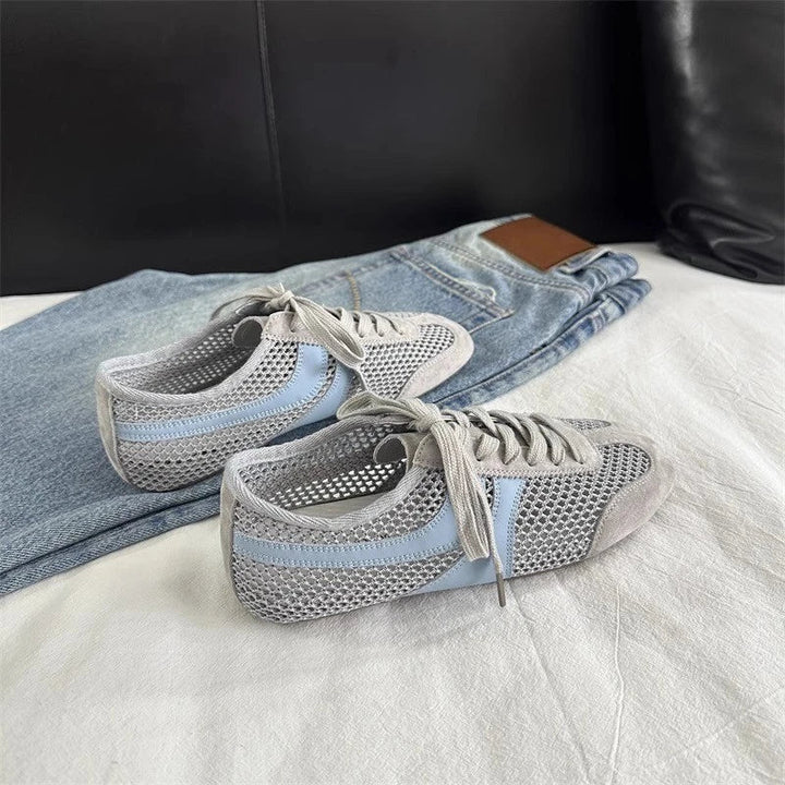 Pair of gray sneakers with blue stripes on a bed with jeans.
