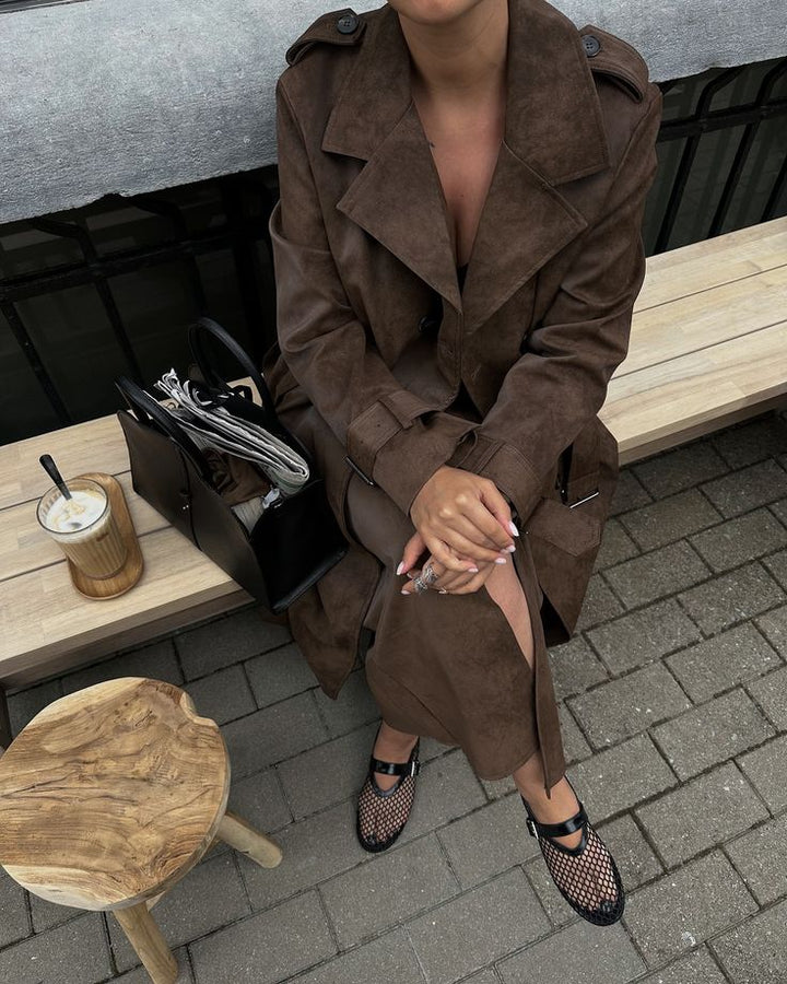 Person wearing a brown trench coat sitting at an outdoor cafe.
