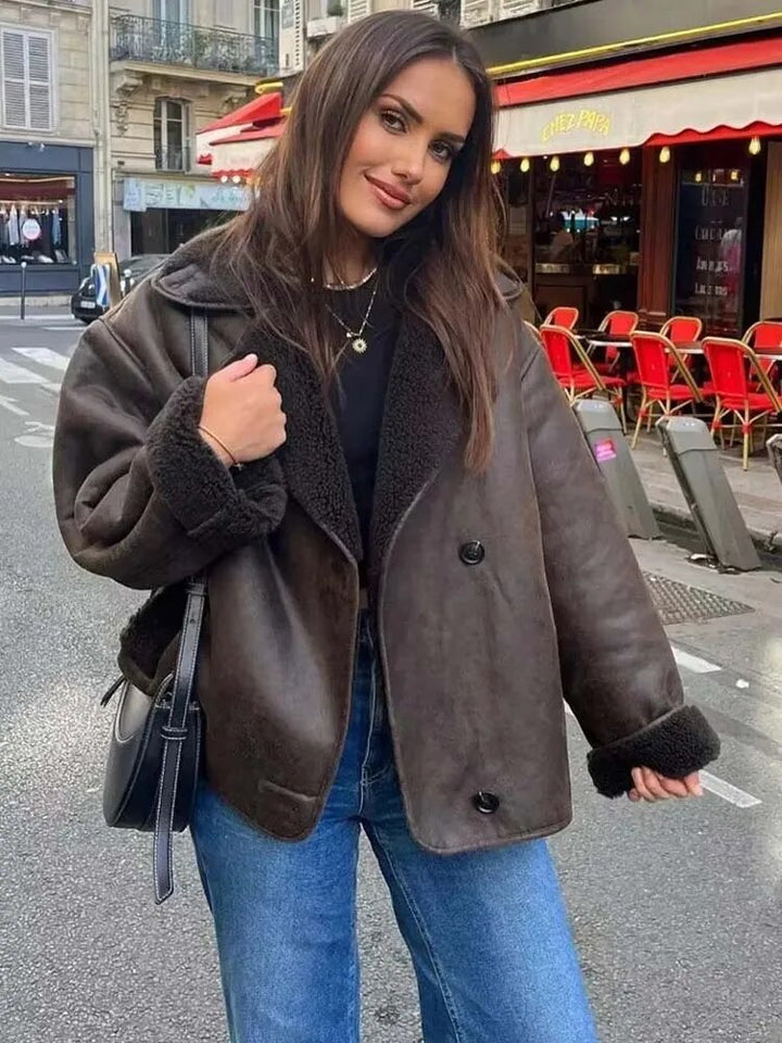 Woman wearing a brown leather jacket and blue jeans on a city street.
