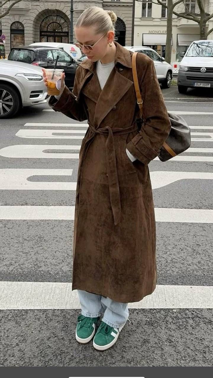 Person wearing a brown coat crossing a street with cars in the background