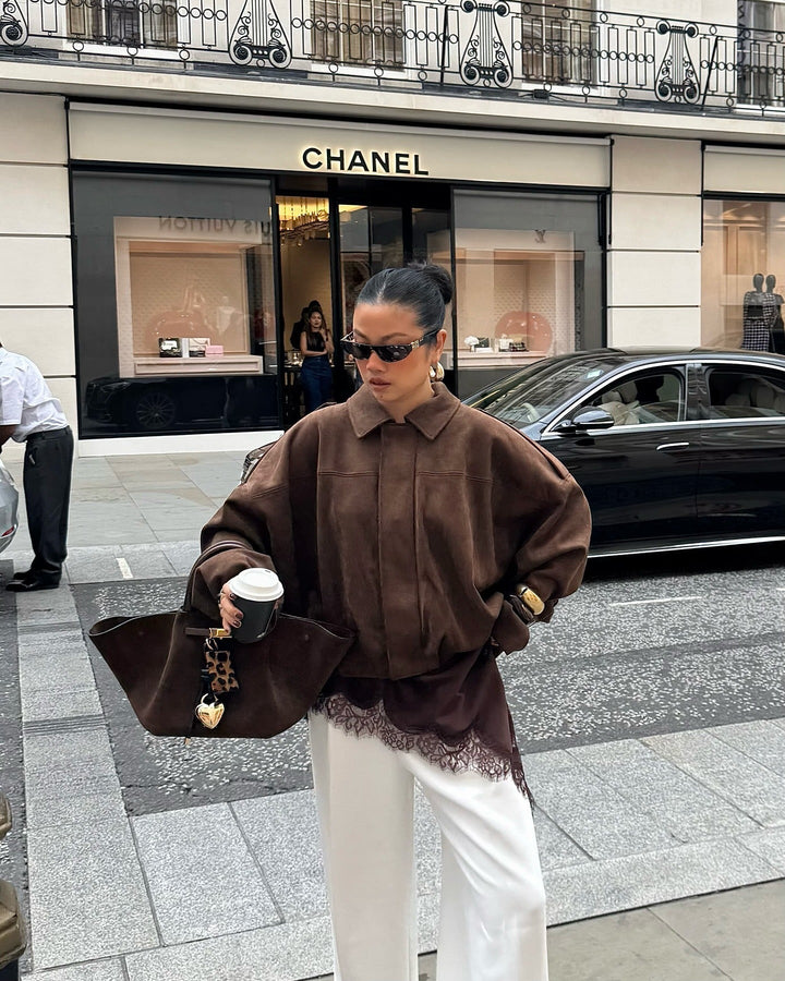 Person in a brown outfit with a large handbag walking on a street in front of a Chanel store.