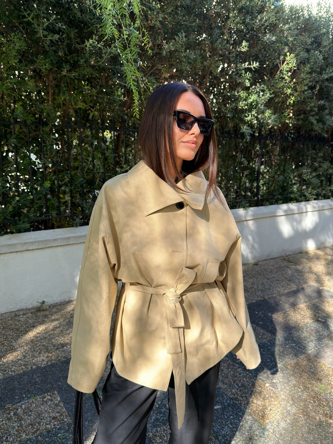 Woman wearing a beige trench coat and sunglasses outdoors.