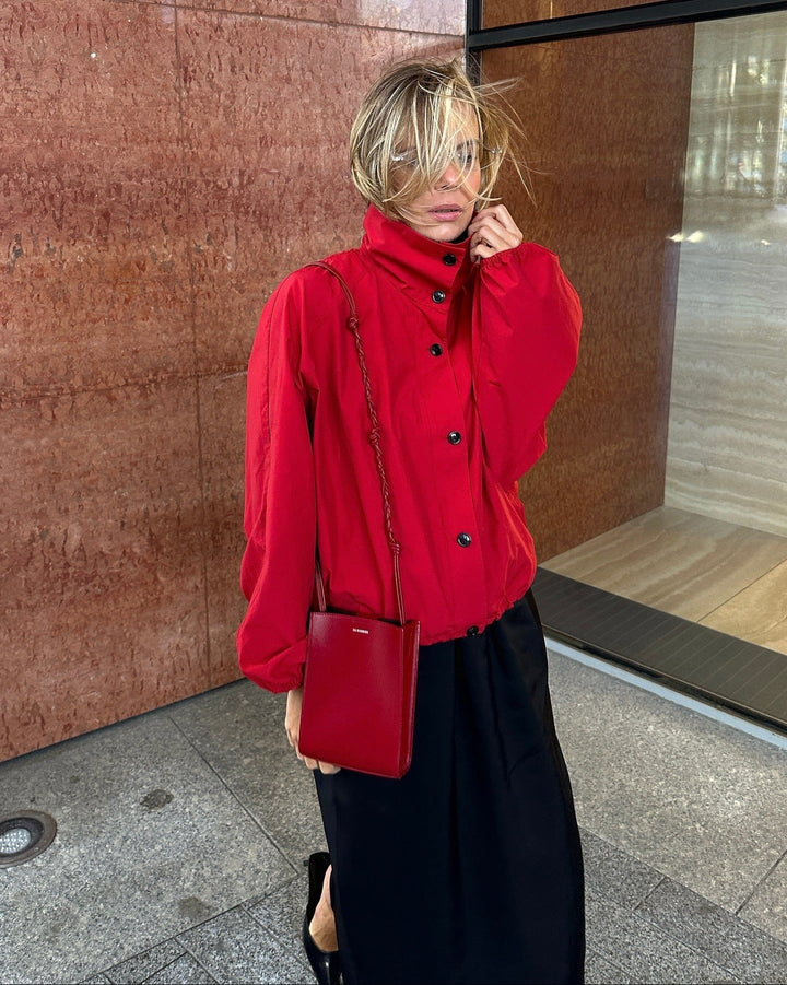 Person wearing a red coat and black skirt standing against a brown wall.