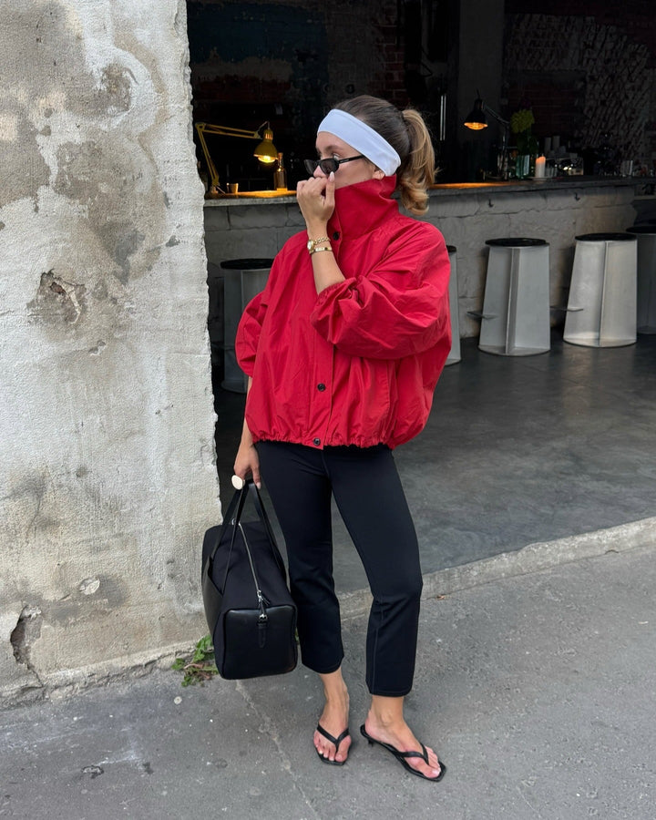 Person wearing a red jacket and black pants standing against a textured wall.