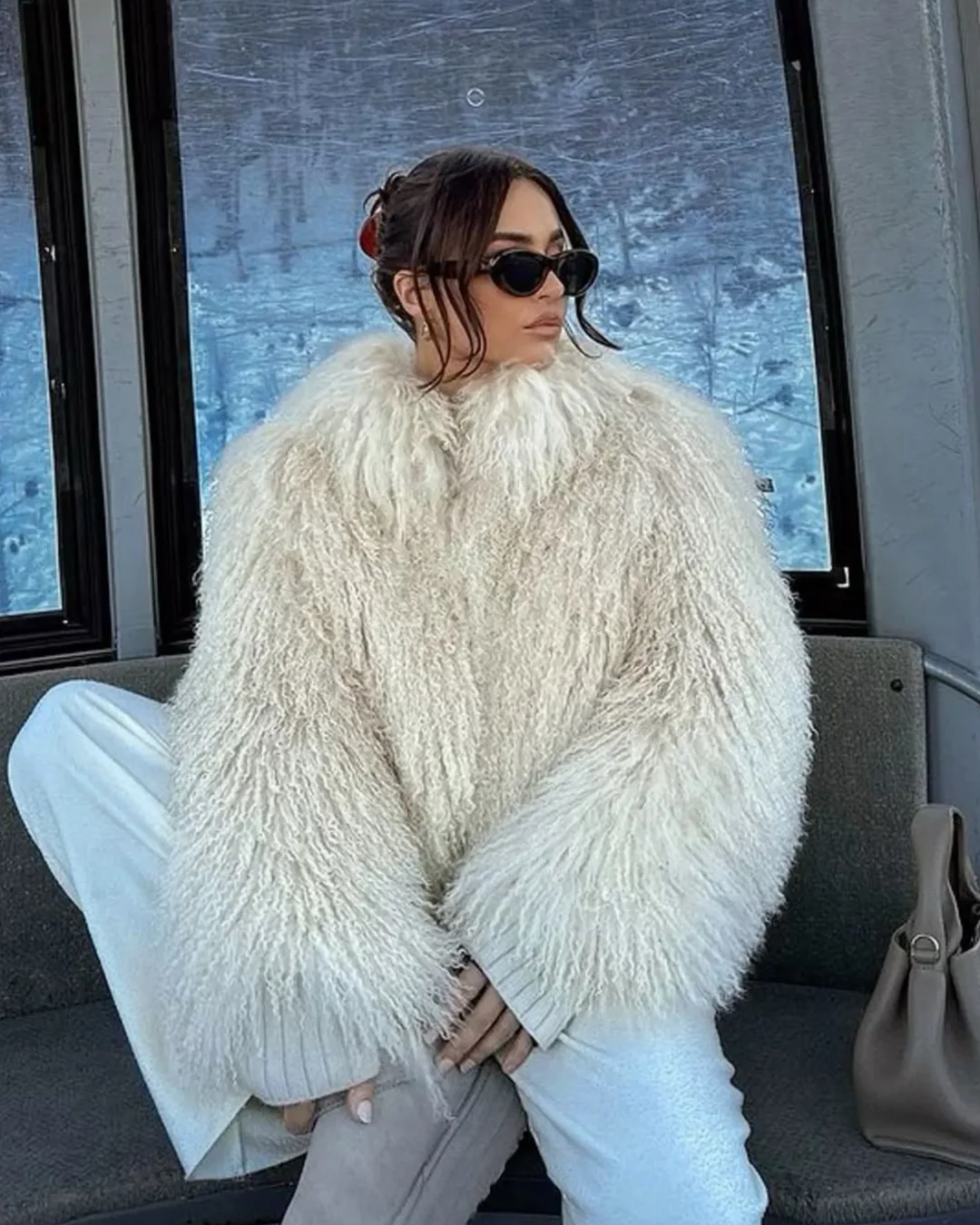 Person wearing a fluffy white coat sitting inside a vehicle with a snowy landscape outside.