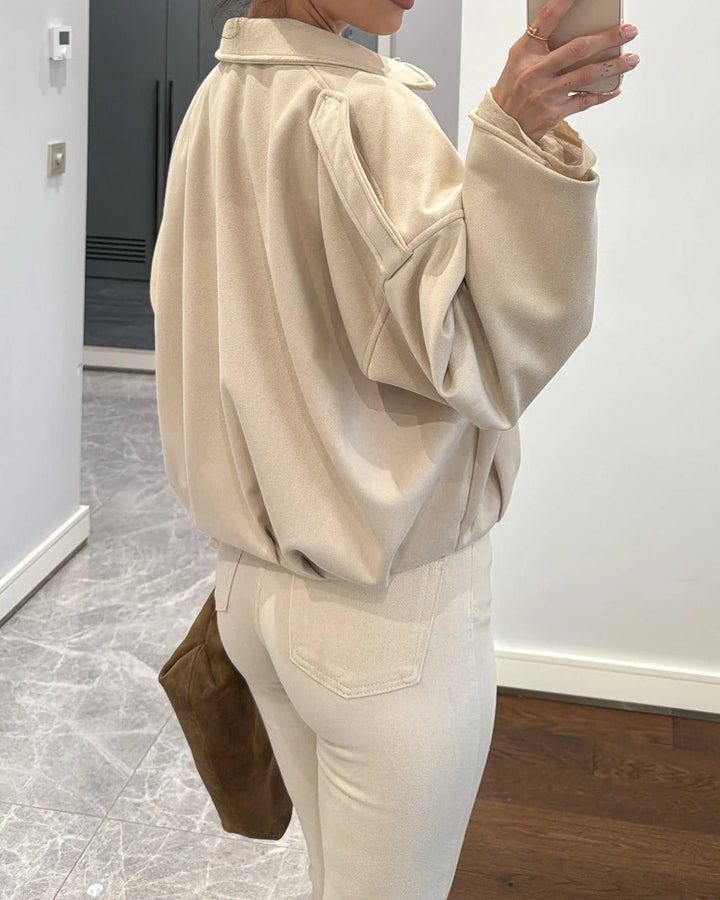 Person wearing a beige jacket and white pants in an indoor setting.